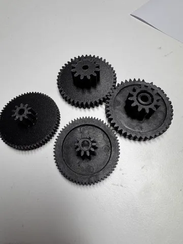 Quatre engrenages noirs imprimés en 3D, pièces de remplacement posées sur une table blanche