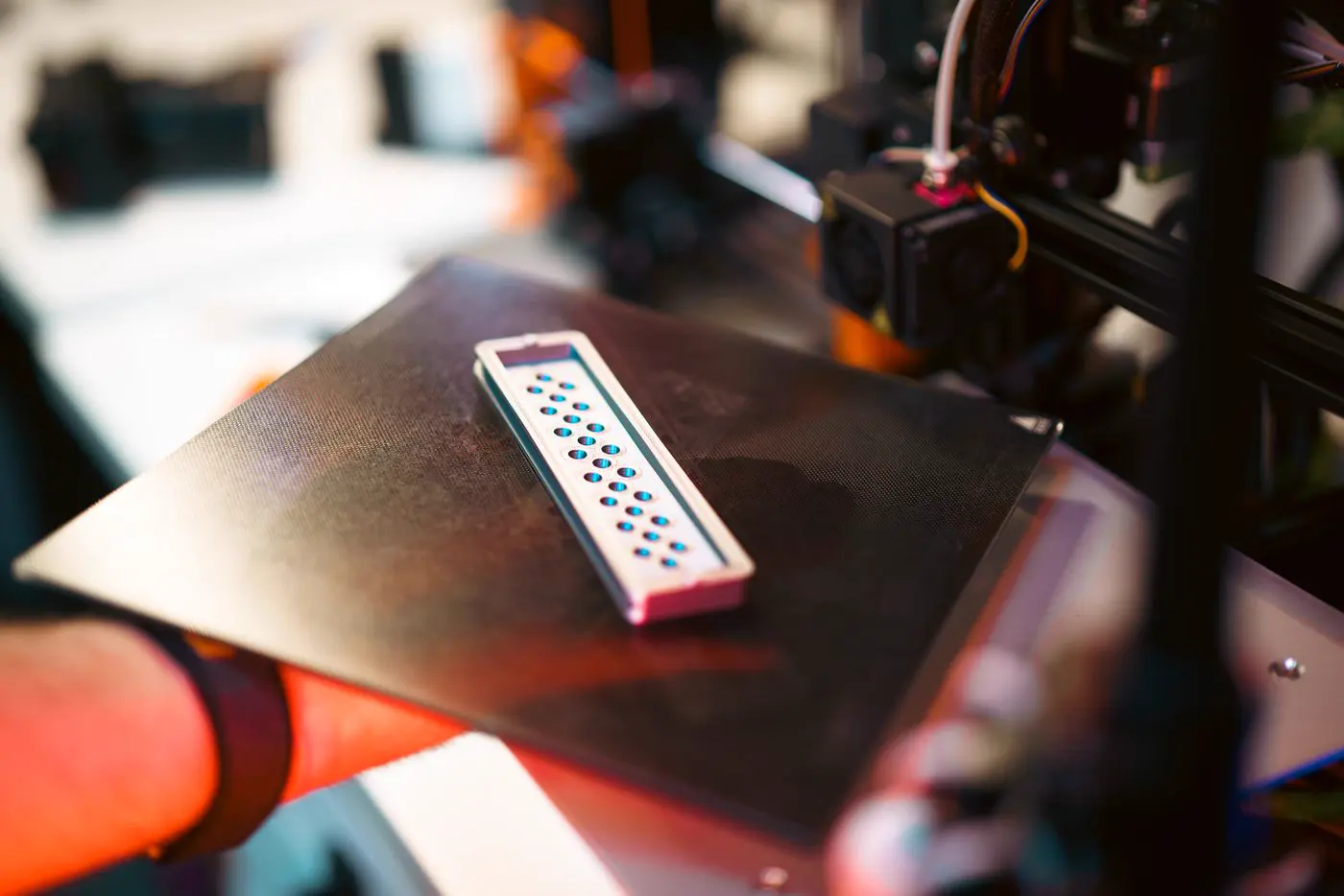 Une pièce rectangulaire ajourée, tout juste imprimée, posée sur le plateau d'une imprimante 3D