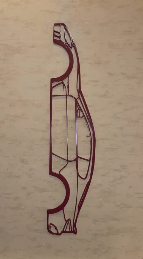 Silhouette filaire d'une voiture de sport imprimée en 3D, rouge, fixée sur un panneau de bois clair